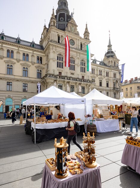 Blick auf den Ostermarkt in Graz mit Holzständen und dem Rathaus im Hintergrund. | © Graz Tourismus  - Harry Schiffer