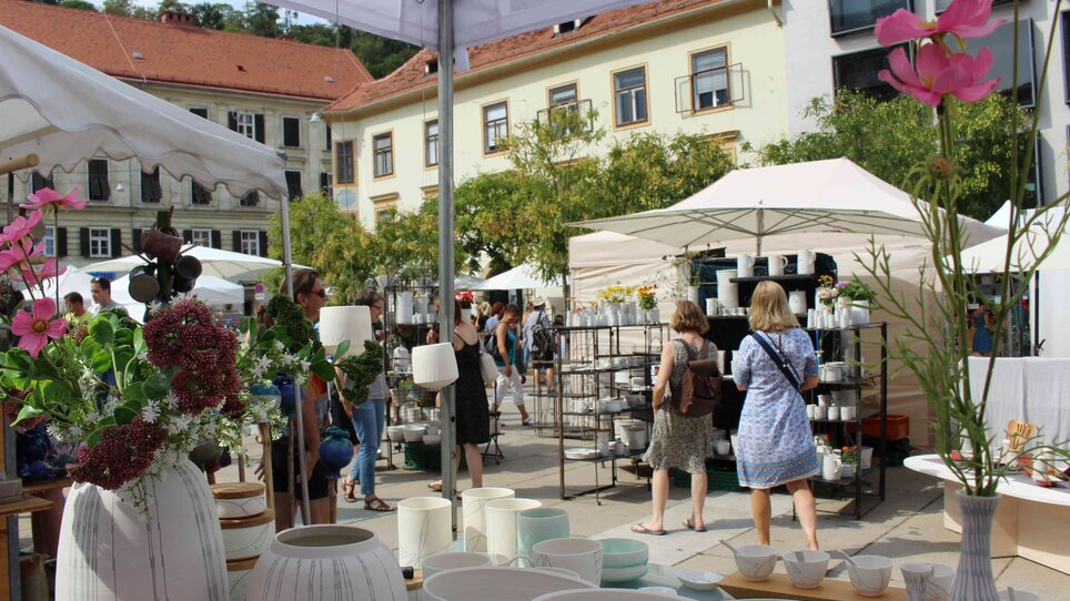 Visitatori esplorano il mercato della ceramica con ceramiche e piante.