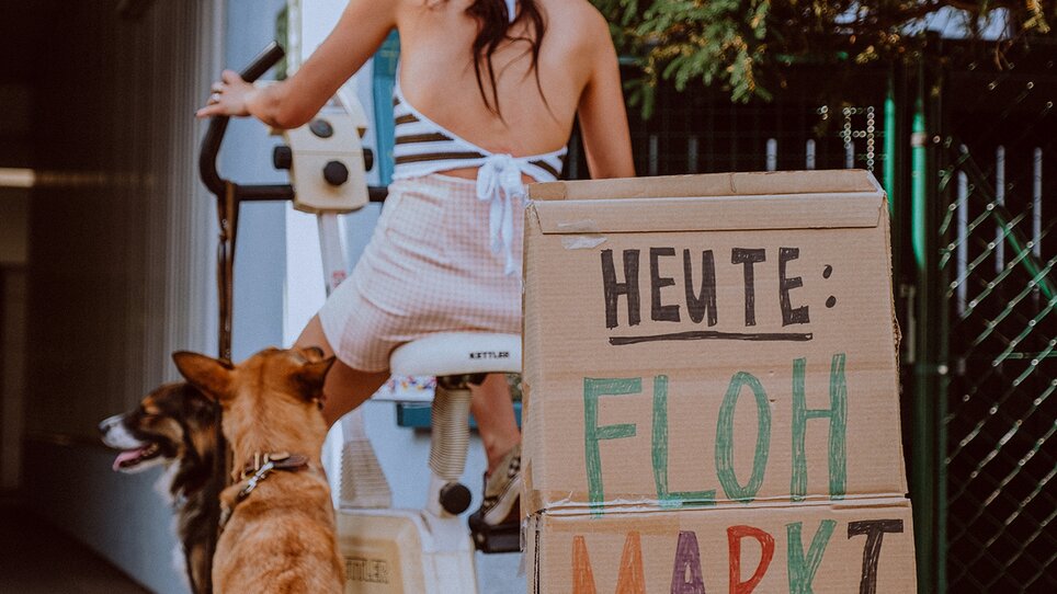 Donna con cane nel cortile con cartello per mercatino delle pulci dalle 8 alle 19. | © Stella