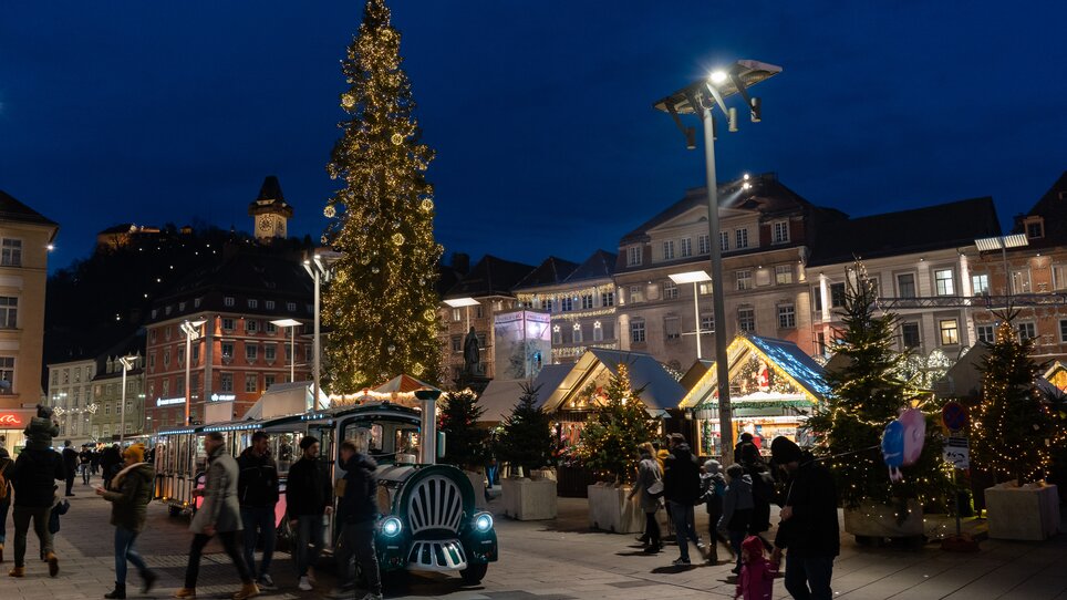 Beleuchteter Christbaum und Adventmarkt in Graz mit Grazer Uhrturm im Hintergrund. | © carnet d'escapades_Laurène Philippot