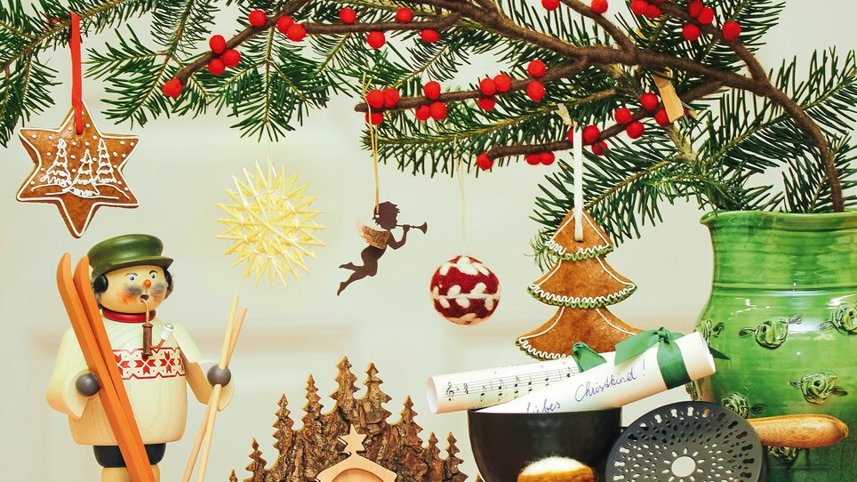 Un tavolo decorato festosamente con ornamenti natalizi, una figura di legno e rami verdi | © VK Stmk