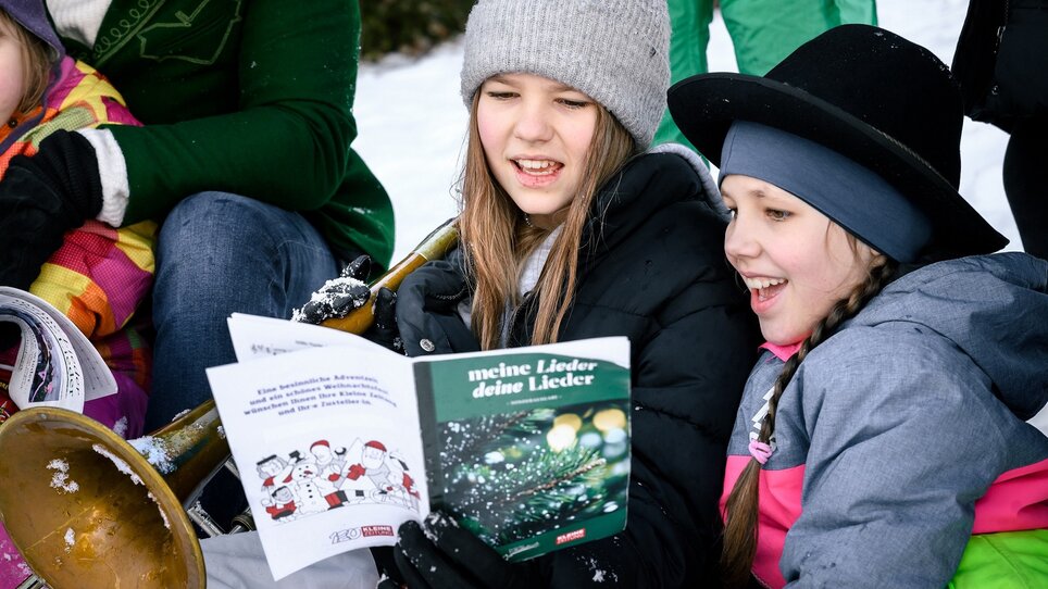Zwei Mädchen freuen sich beim Singen von Weihnachtsliedern im Schnee. | © Ulrike Rauch