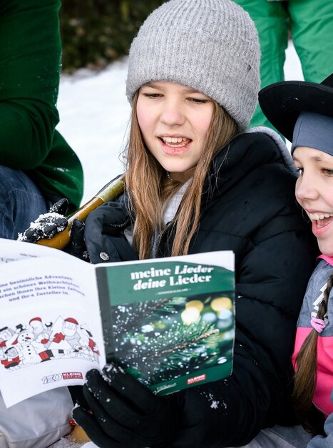 Zwei Mädchen freuen sich beim Singen von Weihnachtsliedern im Schnee. | © Ulrike Rauch