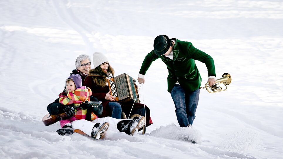 Eine Familie im Schnee sitzt auf einem Schlitten und spielt Musik. | © Ulrike Rauch