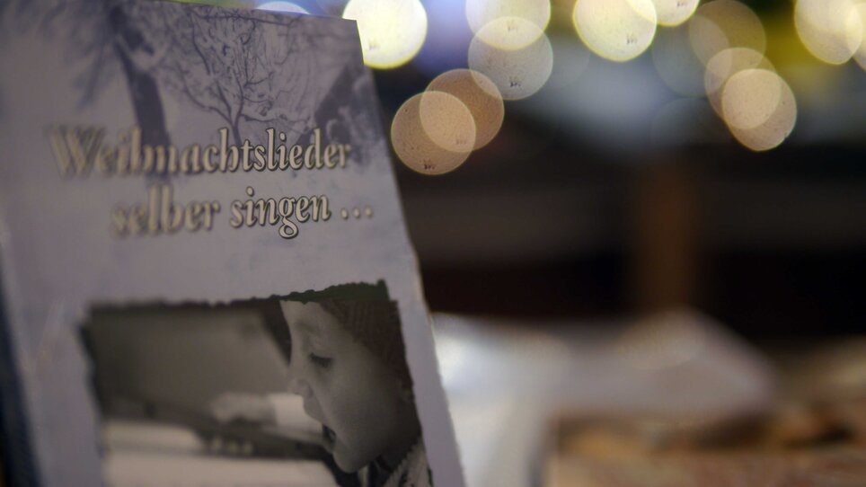 Ein Buch mit dem Titel 'Weihnachtslieder selbst singen...' und einem Kind, das ein Notenblatt betrachtet. | © Steirisches Volksliedwerk