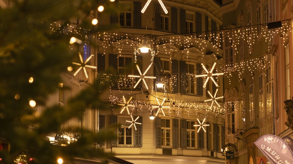 Beleuchtete Gasse in Graz mit Weihnachtslichtern und Sternen, Menschen beim Flanieren. | © Vincent Croce