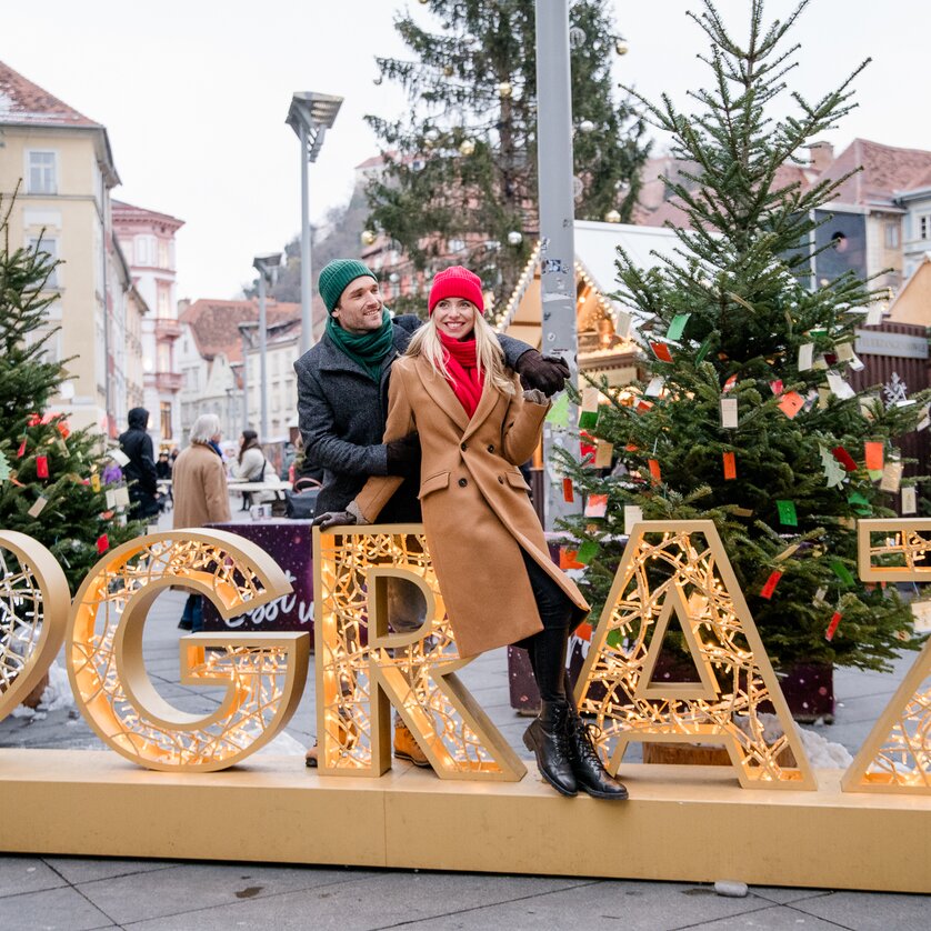 Advent in Graz I Selfie-Spot am Hauptplatz | © Graz Tourismus - Mias Photoart Paar posiert vor beleuchteter Graz-Dekoration im Weihnachtsmarkt. | © Graz Tourismus - Mias Photoart