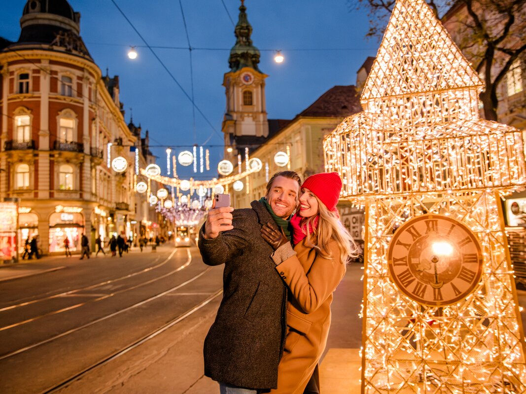 Pärchen macht ein Selfie vor beleuchtetem Uhrenturm in Graz. | © Graz Tourismus - Mias Photoart