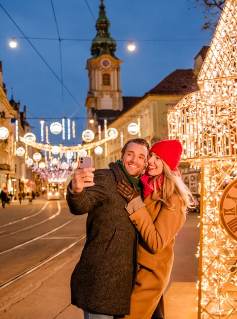 Pärchen macht ein Selfie vor beleuchtetem Uhrenturm in Graz. | © Graz Tourismus - Mias Photoart