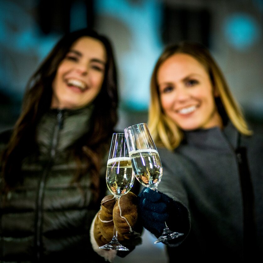 Advent in Graz I Winter in der Steiermark | © Graz Tourismus - Tom Lamm Zwei Frauen halten Sektgläser in der Nacht und lächeln. | © Graz Tourismus - Tom Lamm