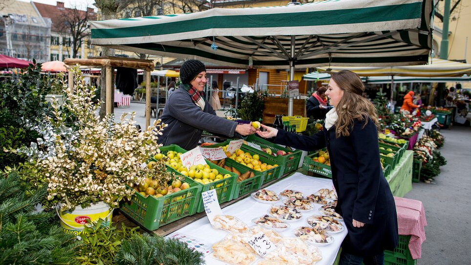 On the market in Graz, a woman exchanges fresh fruit with a vendor. | © Graz Tourismus - Tom Lamm