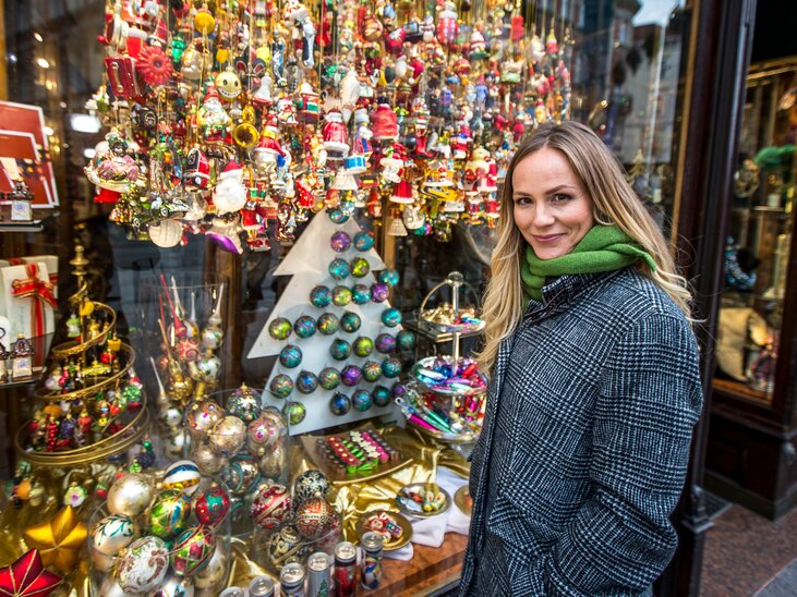 A woman stands in front of a shop window decorated for Christmas in Graz. The window displays colorful ornaments and Christmas figures. | © Graz Tourismus - Tom Lamm