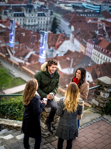Eine Gruppe junger Leute steht am Schlossberg und unterhält sich mit Blick über die Stadt. | © Graz Tourismus - Tom Lamm