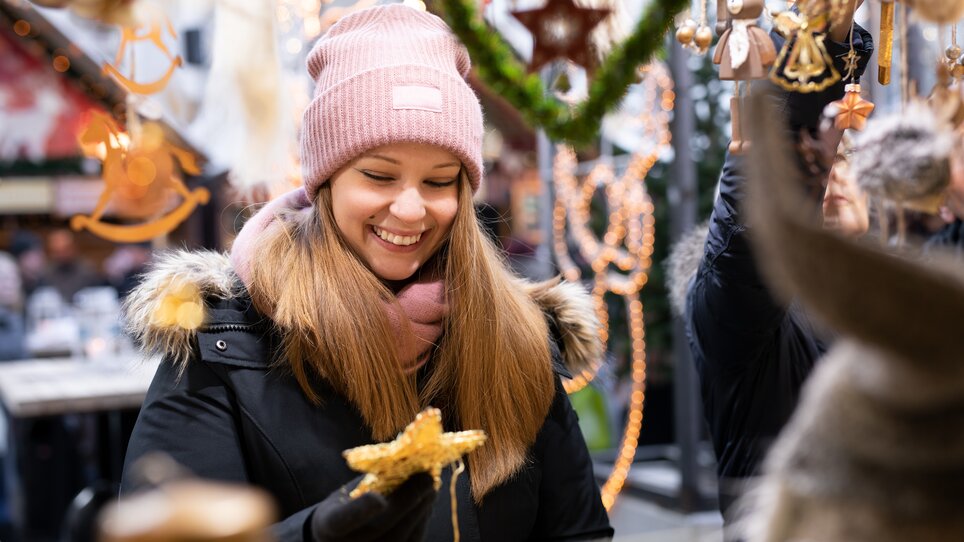 A cheerful young woman holding a star at a Christmas market. | © Graz Tourismus - Katja Stadler