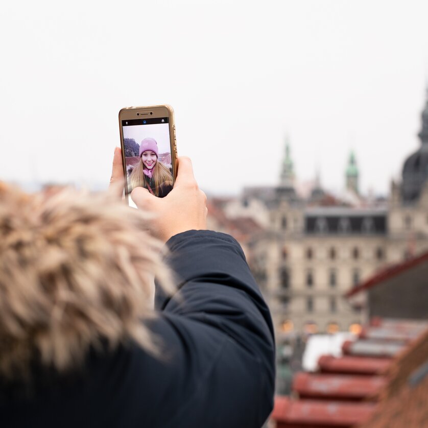 Advent in Graz I Winter in Styria | © Graz Tourismus - Katja Stadler A person takes a selfie with Graz in the background on a cloudy day. | © Graz Tourismus - Katja Stadler