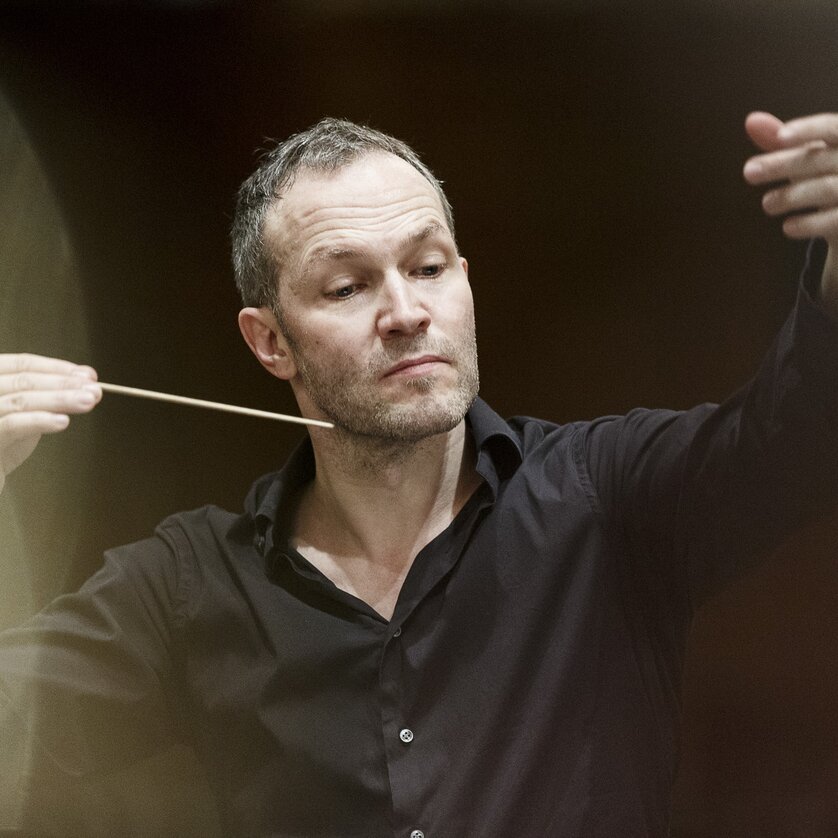 Ein Mann dirigiert mit einem Taktstock, konzentriert in einem Konzertsaal. | © Werner Kmetitsch