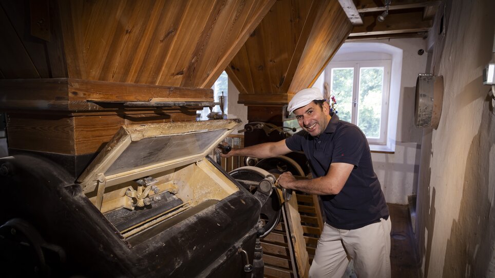 Ein Müller steht an einer großen Mühle und lächelt, während er arbeitet. | © Werner Krug