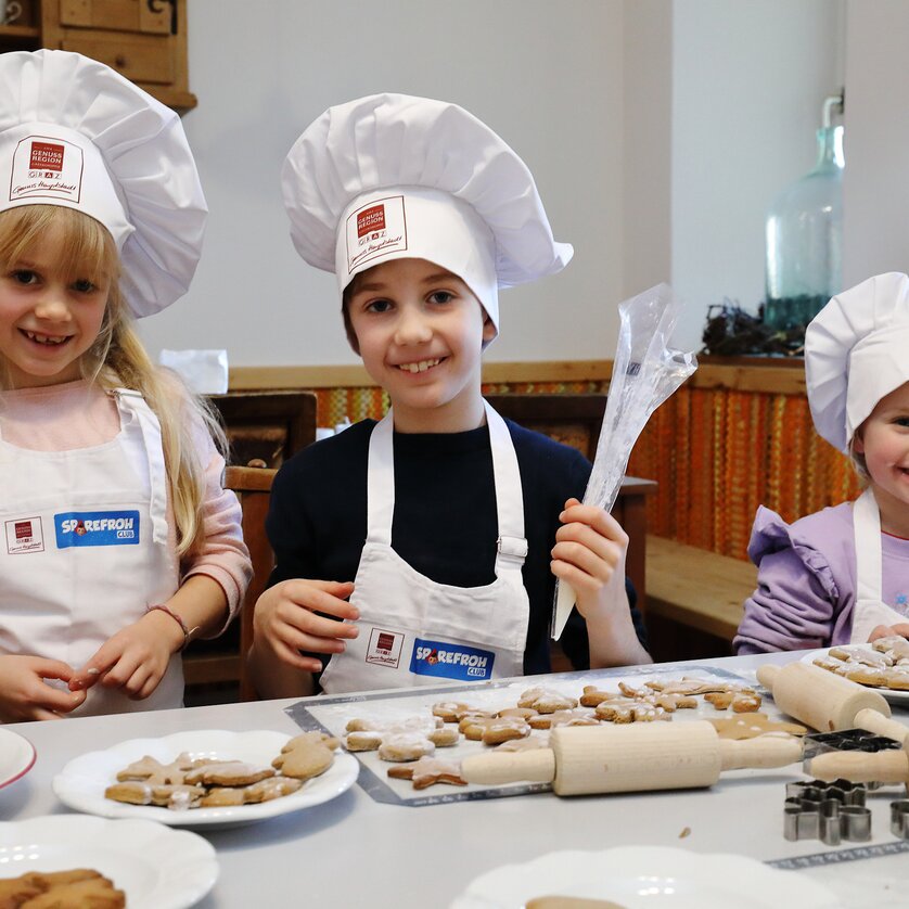 Drei Kinder mit Kochmützen backen Lebkuchen und Weihnachtskekse. | © UMJ - J. J. Kucek