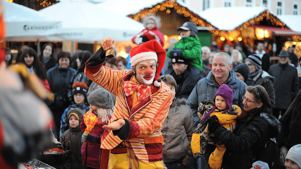 A clown performs for an audience at a Christmas market. | © Foto Jakotopia