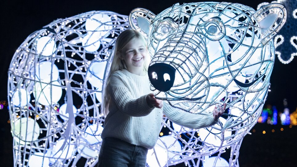Una ragazza si trova accanto a una figura di orso polare illuminata. | © Mathias Kniepeiss