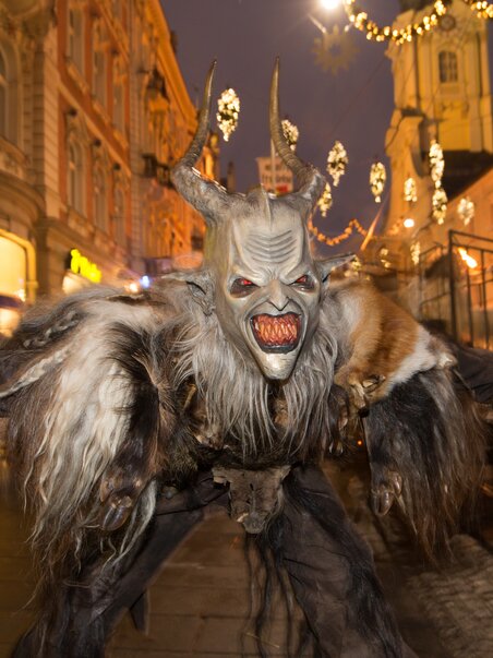 Ein Krampus mit gruseligem Gesicht und zotteliger Kleidung tanzt auf der Straße in Graz. | © Graz Tourismus - Harry Schiffer
