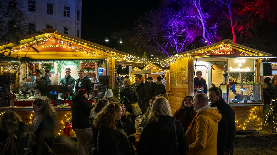 Bancarelle illuminate al mercato di Avvento a Graz, con molte persone che godono dell'atmosfera festiva. | © Peter Hutter