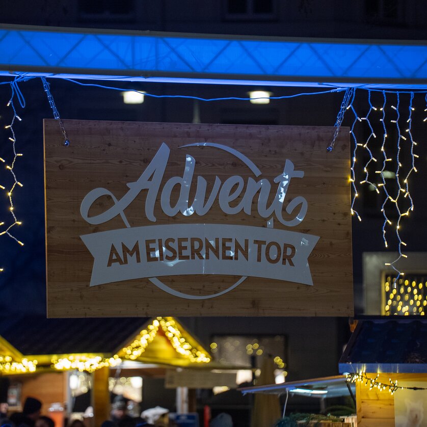 Luci e il cartello con la scritta "Avvento alla Eisernen Tor" a un mercatino di Natale a Graz. | © Peter Hutter