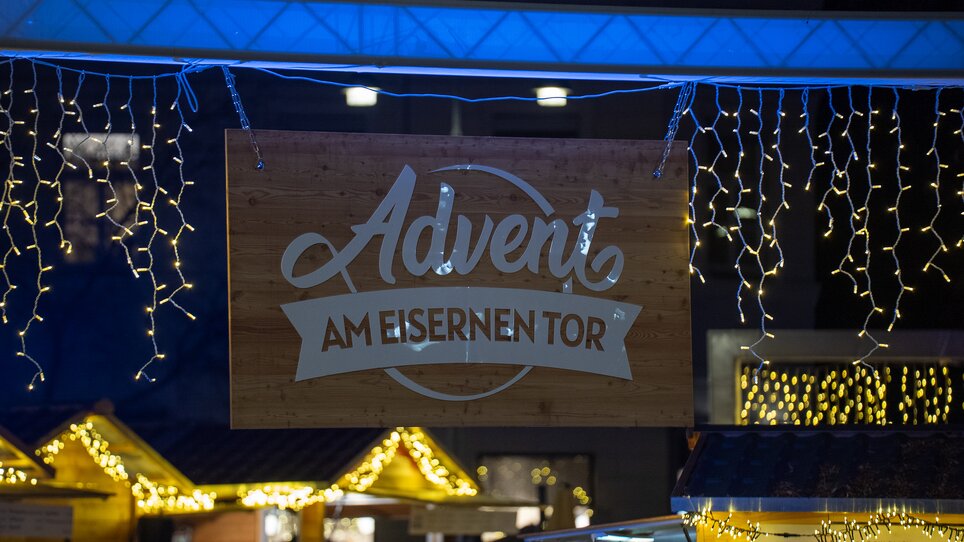 Luci e il cartello con la scritta "Avvento alla Eisernen Tor" a un mercatino di Natale a Graz. | © Peter Hutter