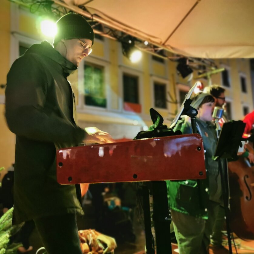 Musiker auf der Bühne beim Adventmarkt, umgeben von festlicher Stimmung. | © Christina Moschitz