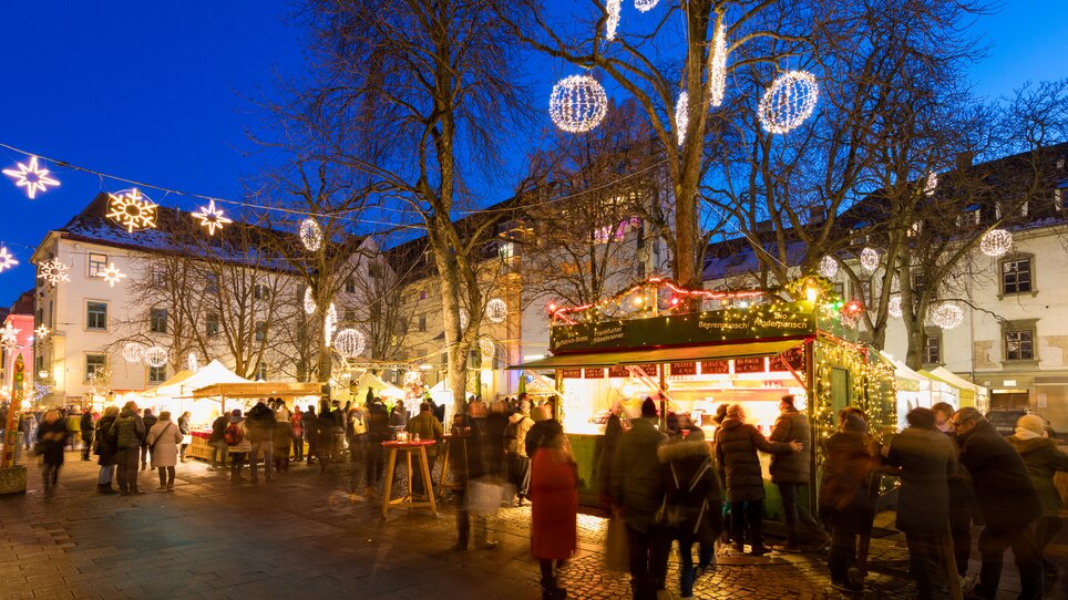 Belebter Weihnachtsmarkt mit Lichtern, Ständen und Menschen in Graz. | © Graz Tourismus - Harry Schiffer
