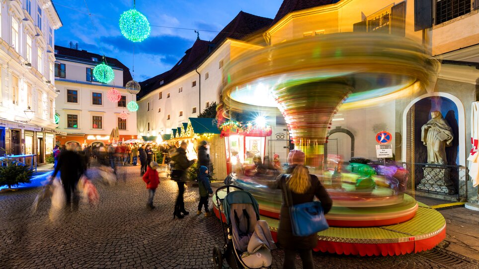 Belebte Szene mit Karussell und Weihnachtsständen im Franziskanerviertel Graz. | © Graz Tourismus - Harry Schiffer