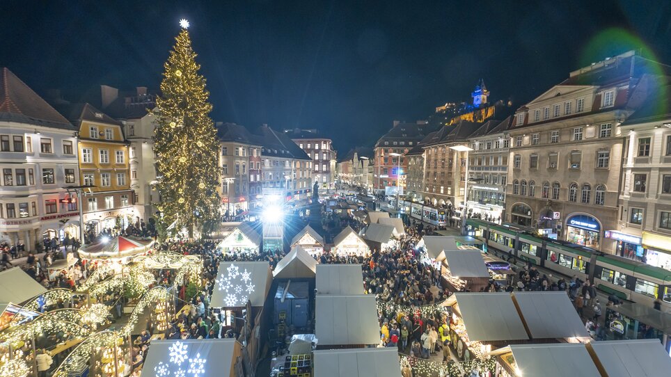 Night view of the Christmas market in Graz with illuminated stalls and large Christmas tree in Hauptplatz. | © Stadt Graz Foto Fischer