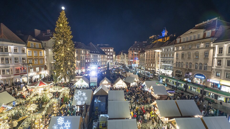 Illuminated Christmas market in Graz with crowds, Christmas tree, and the Graz Clock Tower in the background. | © Stadt Graz - Foto Fischer