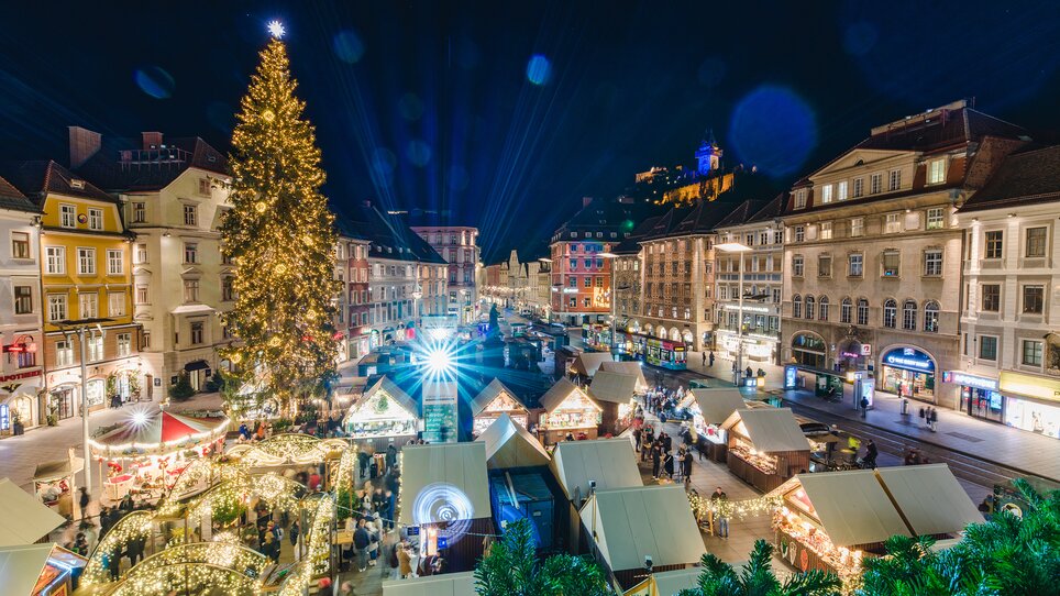 Weihnachtsmarkt in Graz mit festlich beleuchtetem Baum und Grazer Uhrturm im Hintergrund. | © Graz Tourismus - Mias Photoart