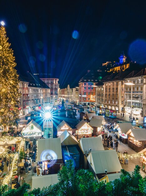 Weihnachtsmarkt in Graz mit festlich beleuchtetem Baum und Grazer Uhrturm im Hintergrund. | © Graz Tourismus - Mias Photoart
