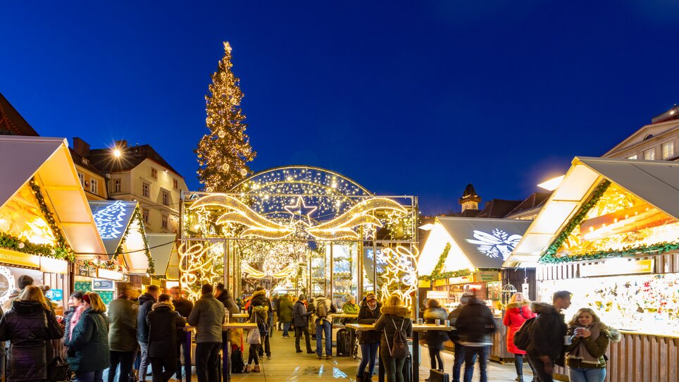 Weihnachtsmarkt in Graz mit stimmungsvoller Beleuchtung, festlich geschmückten Ständen und einem großen Weihnachtsbaum. | © Graz Tourismus - Harry Schiffer
