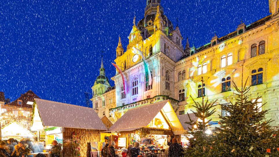 Weihnachtsmarkt mit festlich dekorierten Ständen und Schnee, Rathaus von Graz im Hintergrund. | © Graz Tourismus - Harry Schiffer