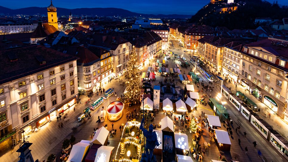 Beleuchteter Christkindlmarkt mit Ständen und Weihnachtsbaum in Graz. | © Graz Tourismus-Harry Schiffer