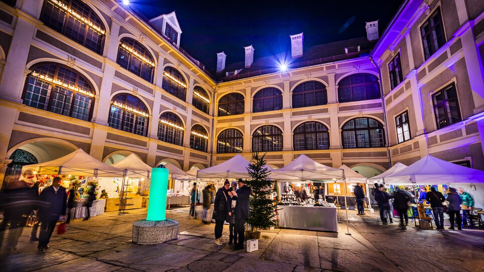 Illuminated courtyard in the Joanneum quarter with stalls and visitors at night. | © Graz Tourismus - Werner Krug
