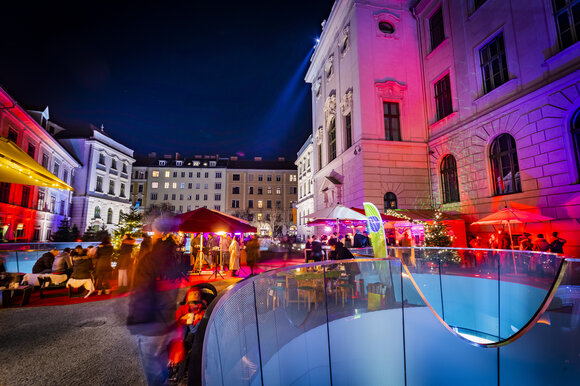 Verschiedene Stände und festliche Beleuchtung im Joanneumsviertel von Graz, umgeben von historischen Gebäuden und einer lebendigen Atmosphäre. | © Graz Tourismus - Werner Krug
