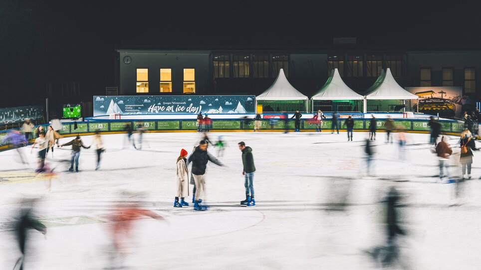 Menschen beim Eislaufen auf einem beleuchteten Eislaufplatz bei Nacht. | © Luke Goodlife