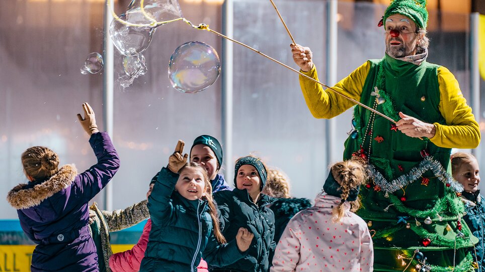 Kinder beim Eislaufen, umgeben von einem Weihnachtsmann im Kostüm. | © Kuro Simon
