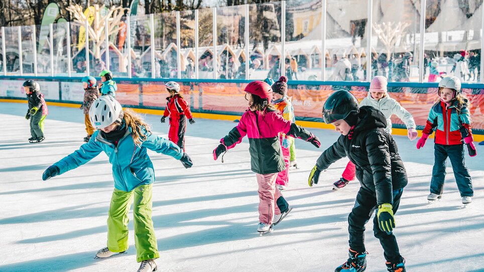 Kinder beim Eislaufen auf einem festlich dekorierten Eislaufplatz. | © Luke Goodlife