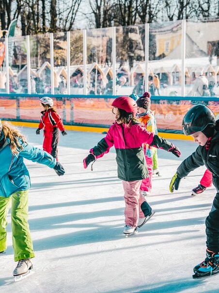 Kinder beim Eislaufen auf einem festlich dekorierten Eislaufplatz. | © Luke Goodlife