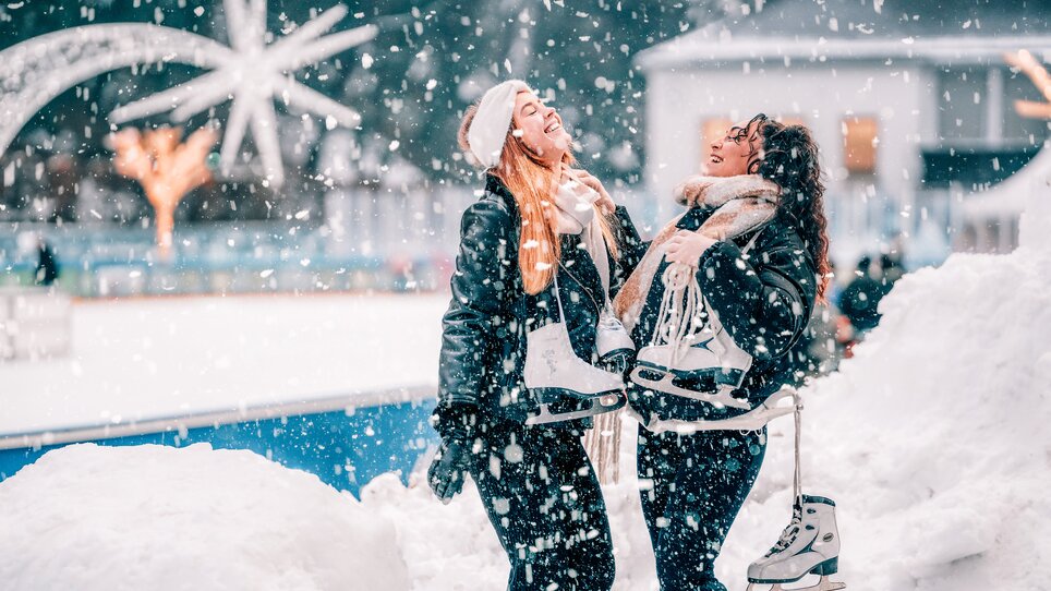 Zwei Frauen lachen und halten Schlittschuhe in einem Winterwunderland. | © Stefan Leitner
