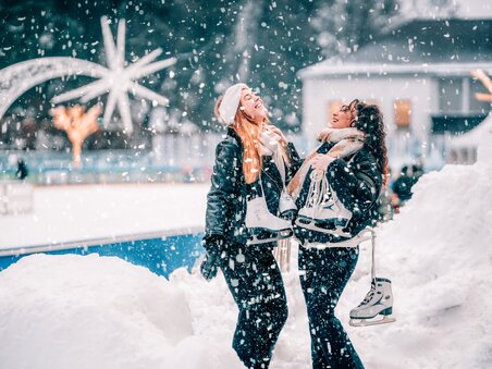 Zwei Frauen lachen und halten Schlittschuhe in einem Winterwunderland. | © Stefan Leitner