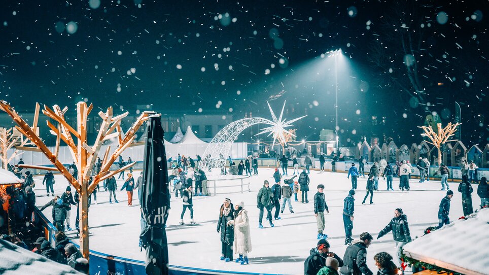 Beleuchteter Eislaufplatz in Graz, umgeben von schneebedeckten Bäumen und Besuchern. | © Stefan Leitner