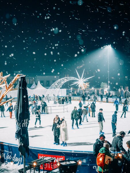 Beleuchteter Eislaufplatz in Graz, umgeben von schneebedeckten Bäumen und Besuchern. | © Stefan Leitner