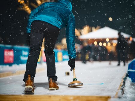 Ein Curling-Spieler auf einem festlich dekorierten Eislaufplatz. | © Stefan Leitner