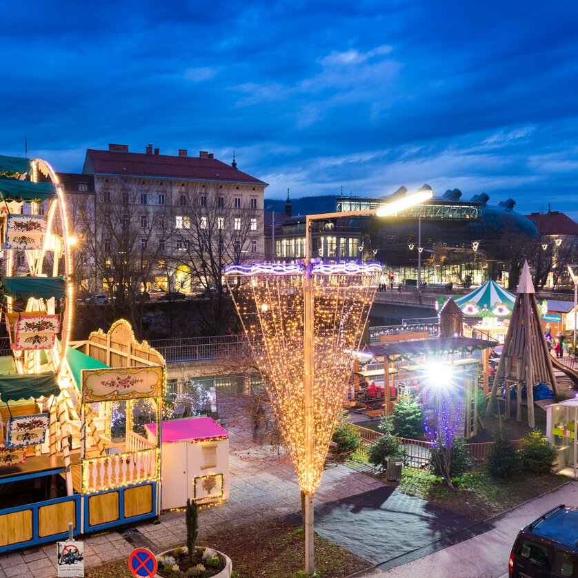 Beleuchtete Fahrgeschäfte und Stände auf dem Adventmarkt in Graz. | © Graz Tourismus-Harry Schiffer
